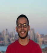 A person wearing glasses and a red shirt stands outdoors with a cityscape in the background during sunset, capturing the moment as local governments manage essential services like water and sewer systems.