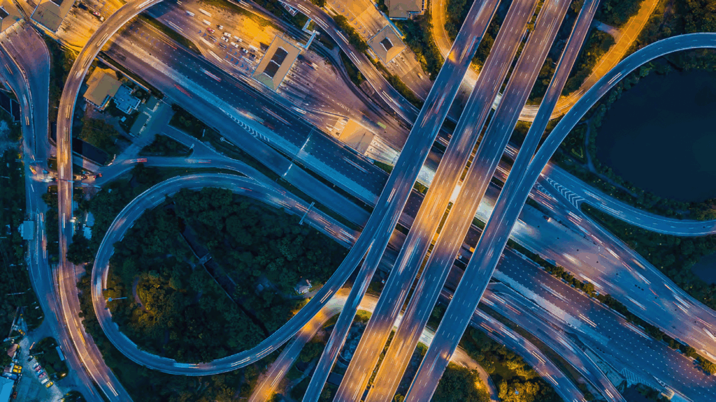 Aerial view of a multi-level highway interchange at night with illuminated streets, moving vehicles, and surrounding greenery—showcasing innovative transportation solutions powered by Bentley Systems.