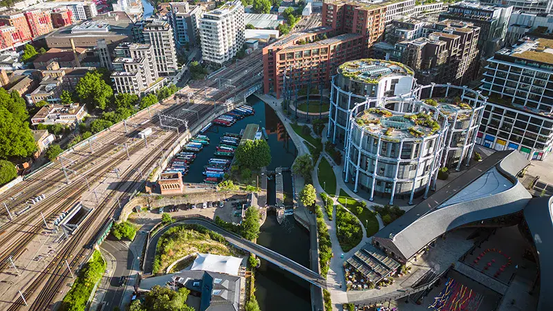 Aerial view of an urban area with train tracks, boats docked in a canal, modern circular buildings, and surrounding city infrastructure.