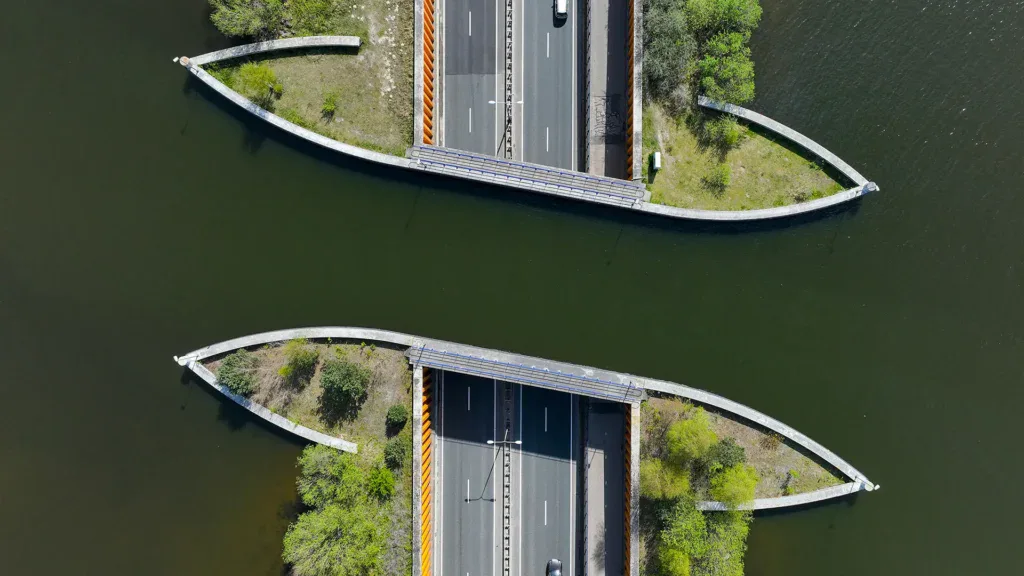 Aerial view of two parallel bridges crossing over water, each carrying a roadway with vehicles, surrounded by greenery.