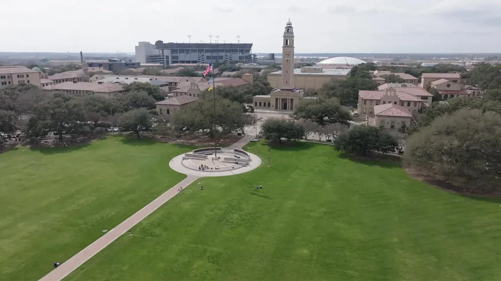 Aerial view of a university campus with a central lawn, flagpole, clock tower, surrounding buildings dedicated to career building, and a stadium in the background.