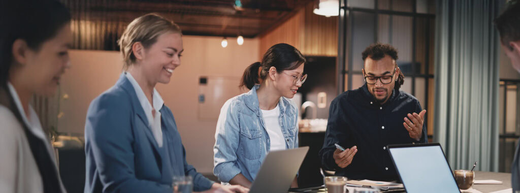 Four people sit at a table with laptops and papers, engaged in a discussion about career development in a modern office setting.