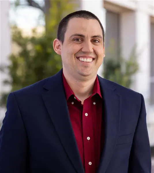 Man wearing a dark blue suit jacket and red shirt smiles