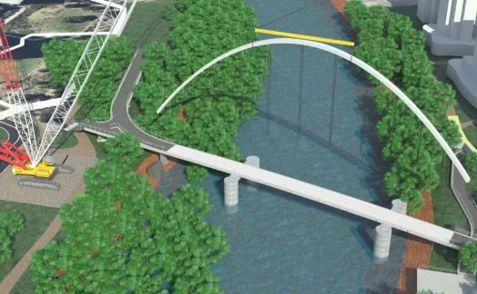 An architectural rendering shows a white arched pedestrian bridge over a river surrounded by trees, with a crane positioned nearby. Buildings and roads are visible in the background, illustrating solid support structures in place.