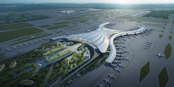 Aerial view of a large, modern airport terminal showcasing innovative design with multiple runways, taxiways, parked airplanes, and surrounding green spaces under a clear sky.