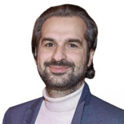 A man with medium-length dark hair and a beard is wearing a suit jacket over a white turtleneck, smiling at the camera against a white background—reflecting the professionalism found in Deep Foundation Design and Deep Foundation Analysis.