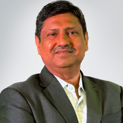 A man smiles while wearing a dark suit jacket over a light collared shirt, standing against a plain light background in this MicroGenesis Partner Spotlight.