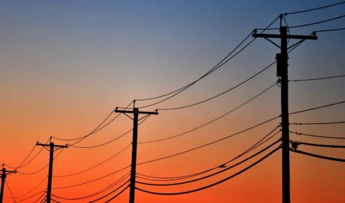 Power lines and utility poles are silhouetted against an orange and blue sunset sky.