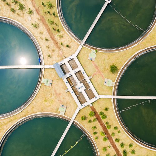 Aerial view of a water treatment plant in draft planning stages, showing five large circular tanks connected by walkways, surrounded by grass and small trees—an essential facility for modern industries.