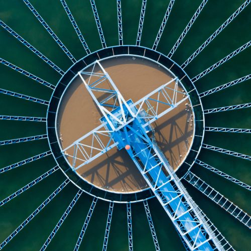 Aerial view of a circular water treatment plant structure with radial metal beams extending from the center over green water, showcasing efficient project delivery.