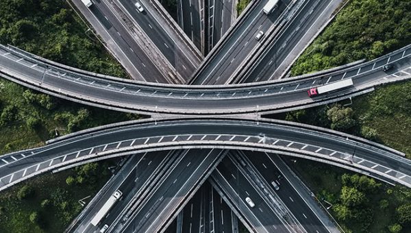 Aerial view of a highway interchange, showcasing Bentley Systems' cutting-edge transportation solutions, with multiple overpasses and vehicles navigating through lush green vegetation.