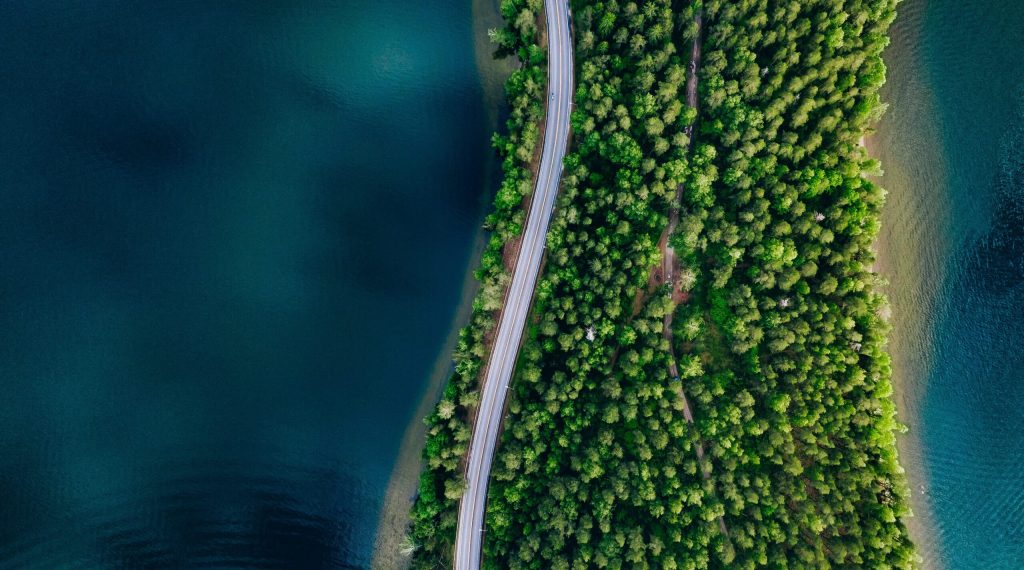 Aerial view of road between green summer forest and blue lake in Finland