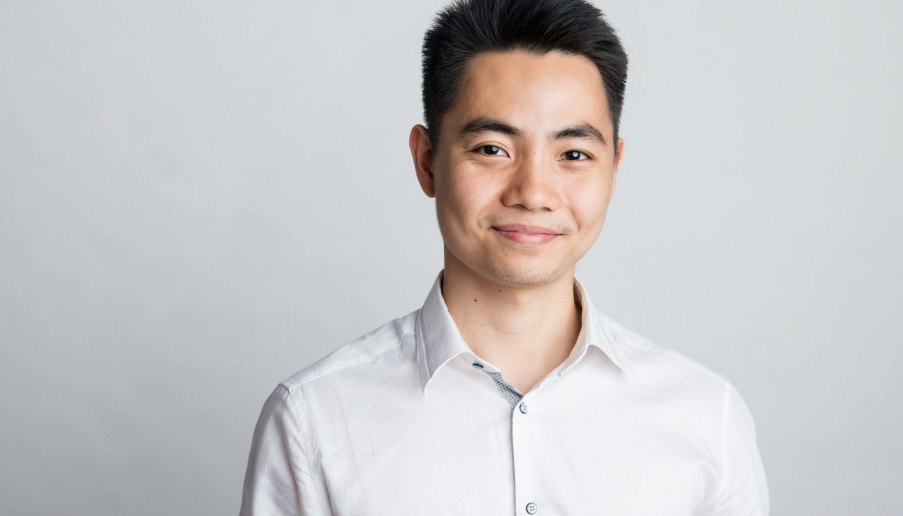 A man with short black hair wearing a white button-up shirt stands against a plain light gray background, smiling slightly for this Bimeco Partner Spotlight.