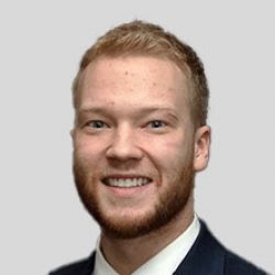 A young man with short, light brown hair and a beard, wearing a dark suit and white shirt, smiles at the camera against a plain gray background—reflecting confidence in fields like AI and Bridge Information Modeling.