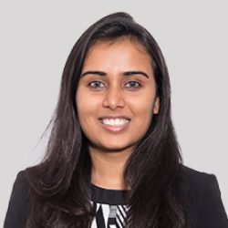 A woman with long dark hair, wearing a black blazer and patterned top, smiles at the camera against a plain light gray background—reflecting confidence in AI-driven BIM solutions.