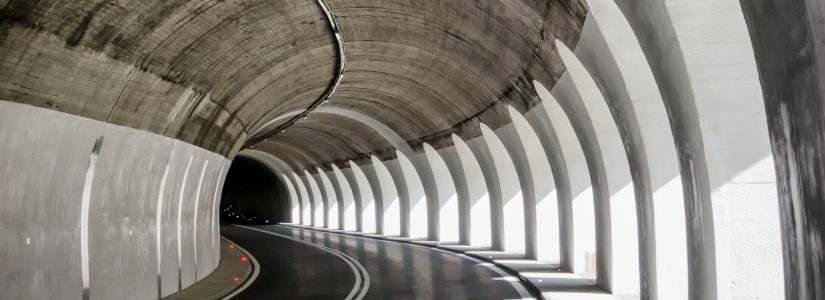 Curved road tunnel with concrete arches and white dividing lines, featuring light and shadow patterns on the walls and pavement—a true architectural spotlight.