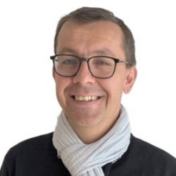 Smiling man wearing glasses, a light-colored scarf, and a dark sweater, standing against a plain white background—perfect for presentations on Deep Foundation Design or tutorials using PLAXIS 3D.