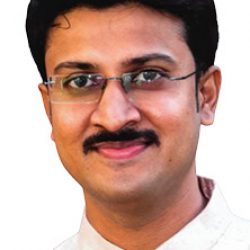 A man with short black hair, a mustache, and glasses is wearing a cream-colored traditional outfit and smiling at the camera, possibly after presenting his work on Geological Modelling.