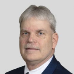 Man with short gray hair, mustache, and wearing a dark suit jacket, white shirt, and tie, posed against a plain light gray background—reflecting a professional involved in BIM and AI technologies.