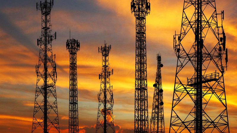 A group of communication towers are silhouetted against a vibrant sunset sky, showcasing their sleek design.