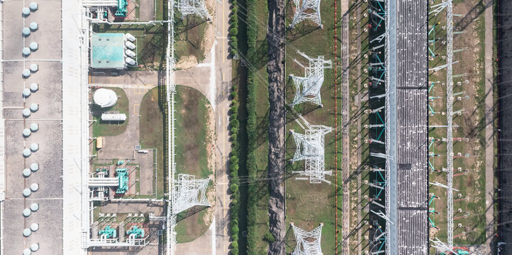 Aerial view of an industrial complex featuring machinery, pipelines, and electric utilities infrastructure, with transmission towers arranged in parallel lines.