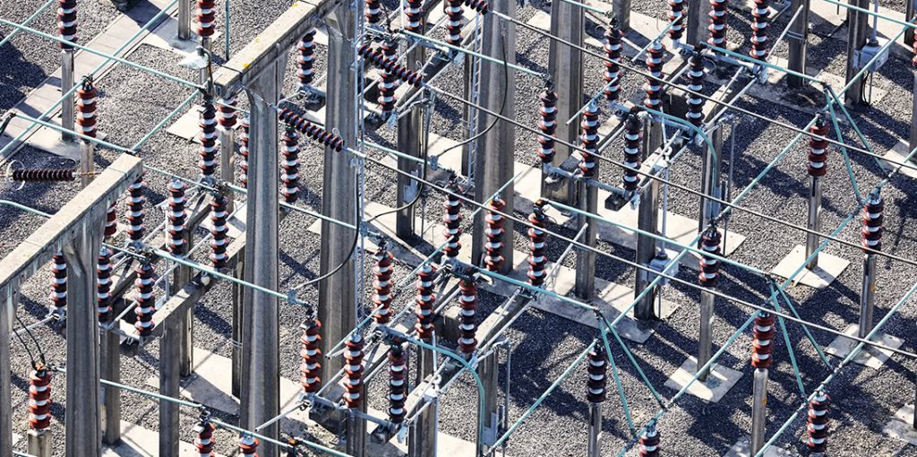 Aerial view of an electrical substation operated by electric utilities, featuring metal structures, insulators, and connecting wires arranged in a grid pattern.