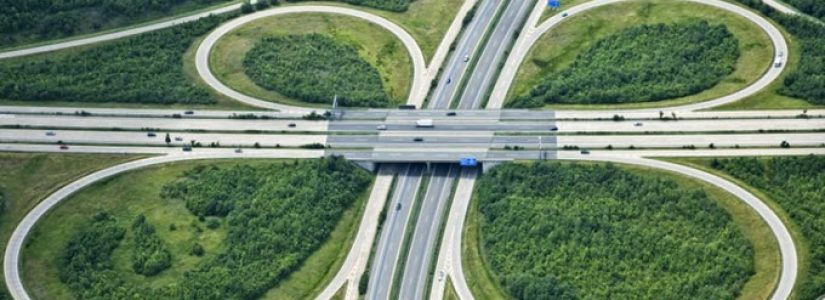 Aerial view of a highway cloverleaf interchange with overpasses, looping ramps, and surrounding green vegetation.