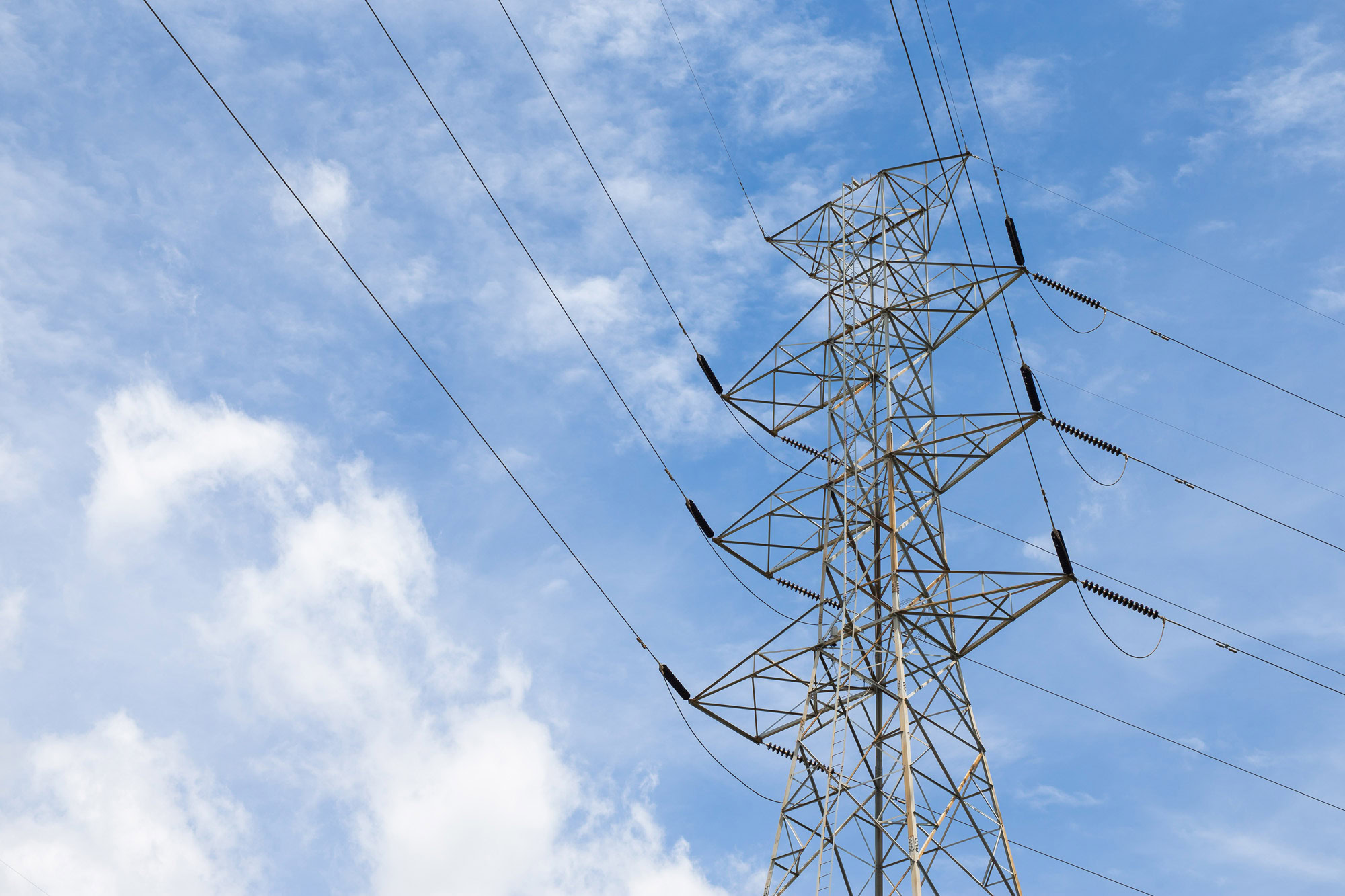 A metal electricity transmission tower with power lines stands tall against a partly cloudy blue sky, showcasing the vital role of electric utilities in delivering reliable electric power.
