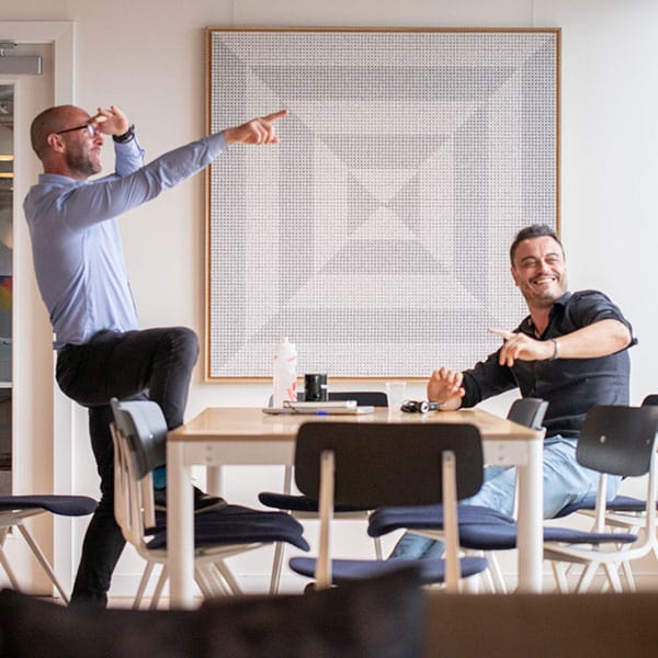 Two guys hanging out by a table laughing and pointing to something