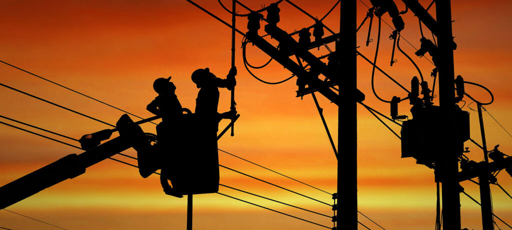 workers analyzing telephone poles back lite from sunset