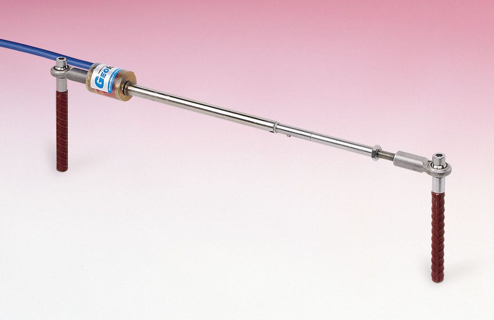 A metal rod with two red textured handles on each end and a blue cable attached at one side, set against a pink and white gradient background.