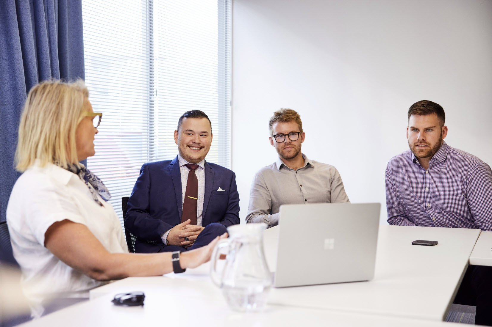 Four people sit at a conference table with a laptop, discussing geotechnical design in a bright office setting.