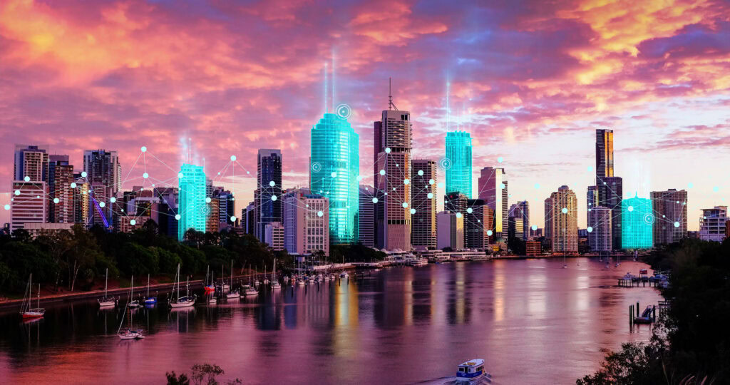 A city skyline during sunset with tall buildings illuminated by turquoise lights and digital connection lines overlayed, reflecting in a calm river with boats docked along the shore, sets the perfect scene for an unforgettable event.