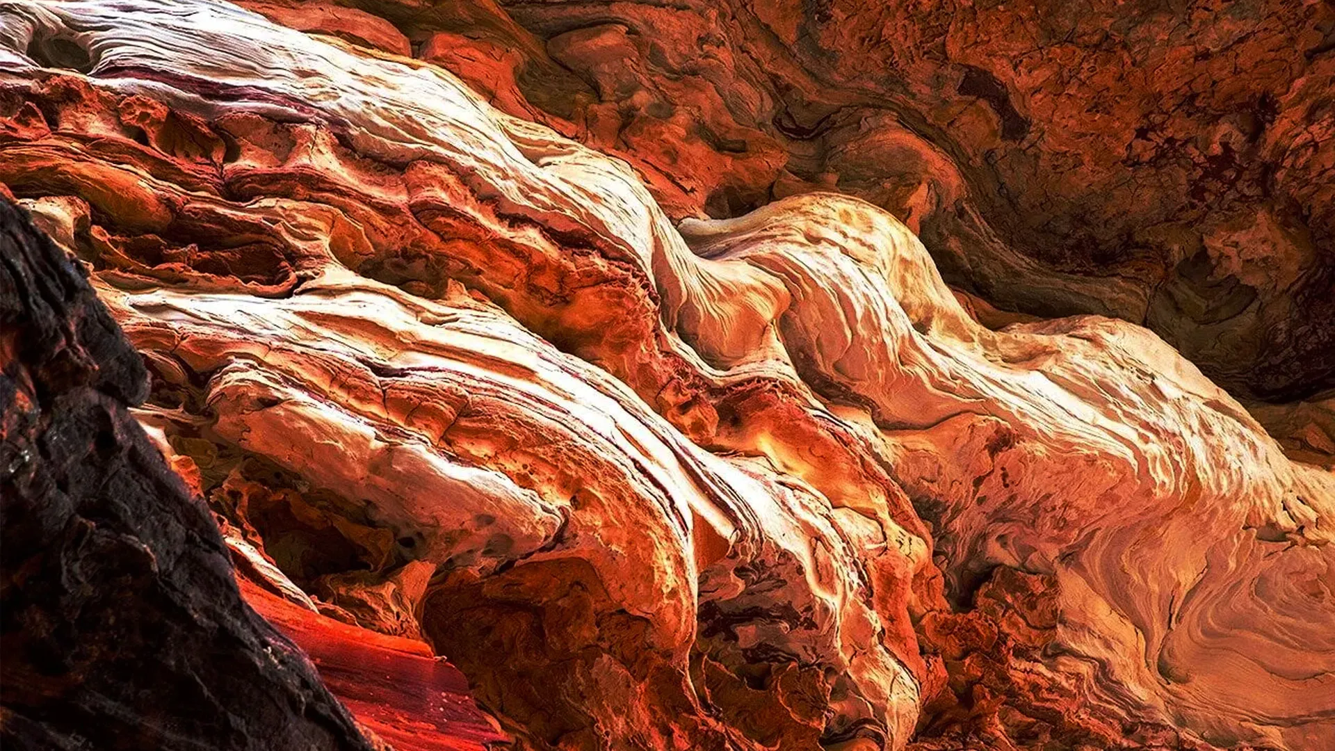 Close-up view of swirling, layered rock formations in shades of red, orange, and cream inside a cave or canyon.