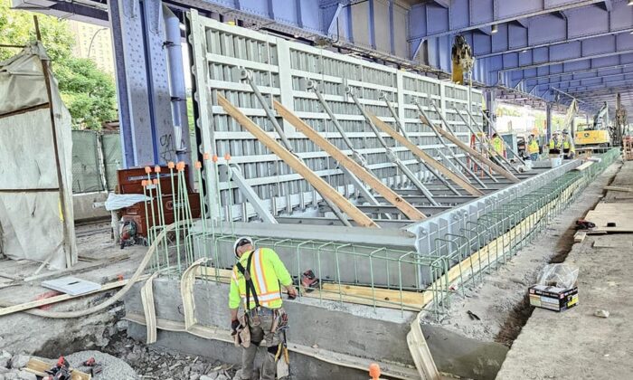 Pracownicy budowy w Nowym Jorku wzmacniają i kontrolują dużą betonową formę pod mostem, z widocznymi stalowymi podporami i tymczasowymi drewnianymi stężeniami, zapewniając odporność na zmiany klimatu w nowoczesnej infrastrukturze.