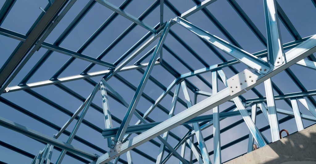 Charpente métallique d'un bâtiment en construction, montrant des poutres se découpant sur un ciel bleu clair.