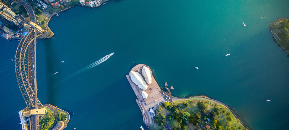 Aerial view of Sydney Opera House with Harbour Bridge and surrounding waters, boats visible, during the Illuminate Sydney event.