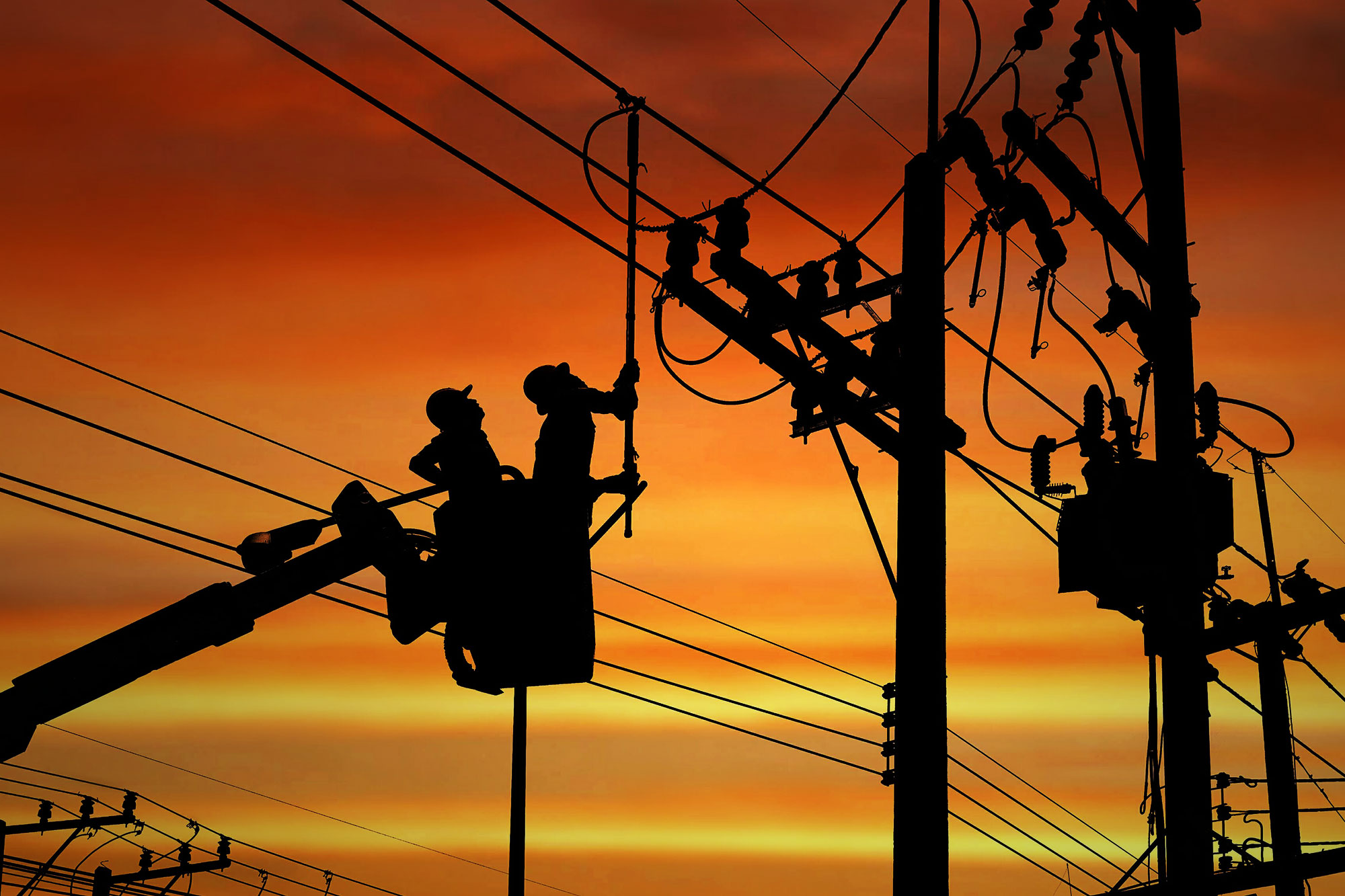 Silhouette two electricians with disconnect stick tool on crane truck are working to install electrical transmission on power pole stock photo