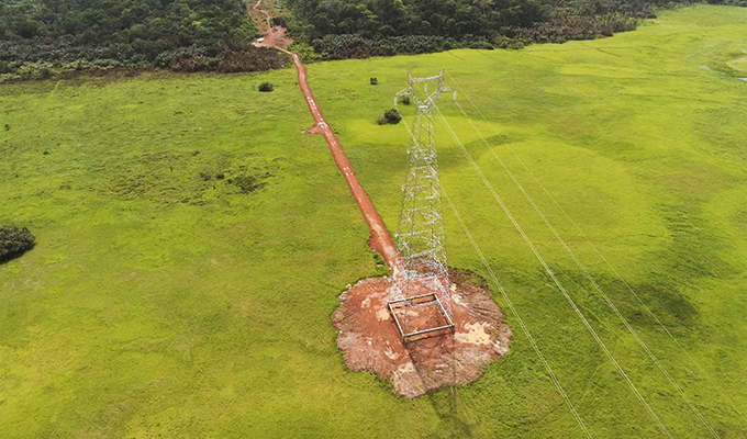 Luftaufnahme eines Strommasts mit Stromleitungen auf einer grünen Wiese.