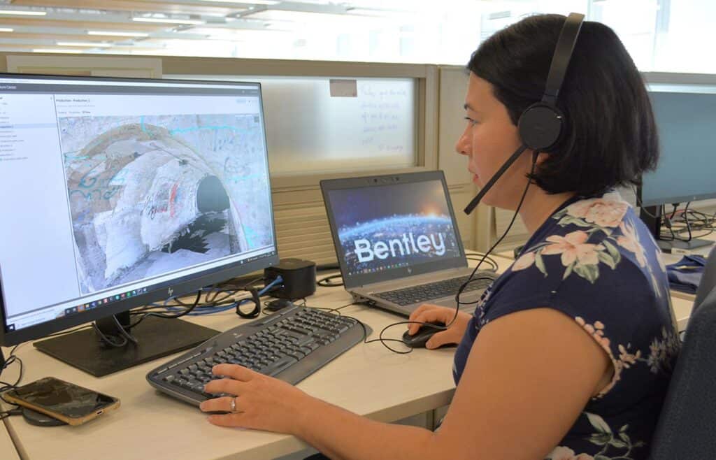 Kobieta siedząca przy biurku, patrząca na program komputerowy i rozmawiająca przez zestaw słuchawkowy