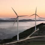 Wind turbines up on a hill with fog in the background