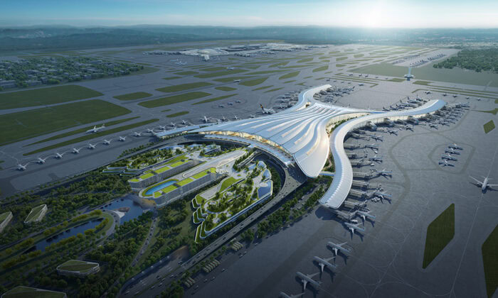 Aerial view of a modern airport terminal with multiple runways, taxiways, and aircrafts parked near gates. The terminal features a sleek, curved design with surrounding greenery and roadways.