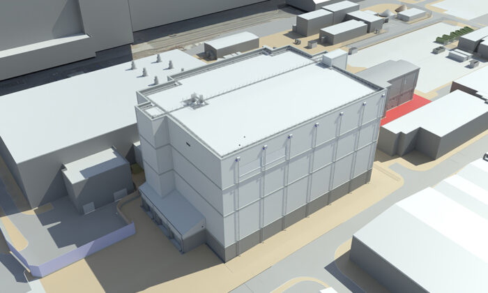 Aerial view of a large, multi-story industrial building surrounded by other buildings and pathways in an industrial area. The building has multiple vents and rooftop equipment.