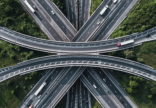 Aerial view of a highway interchange, showcasing Bentley Systems' cutting-edge transportation solutions, with multiple overpasses and vehicles navigating through lush green vegetation.