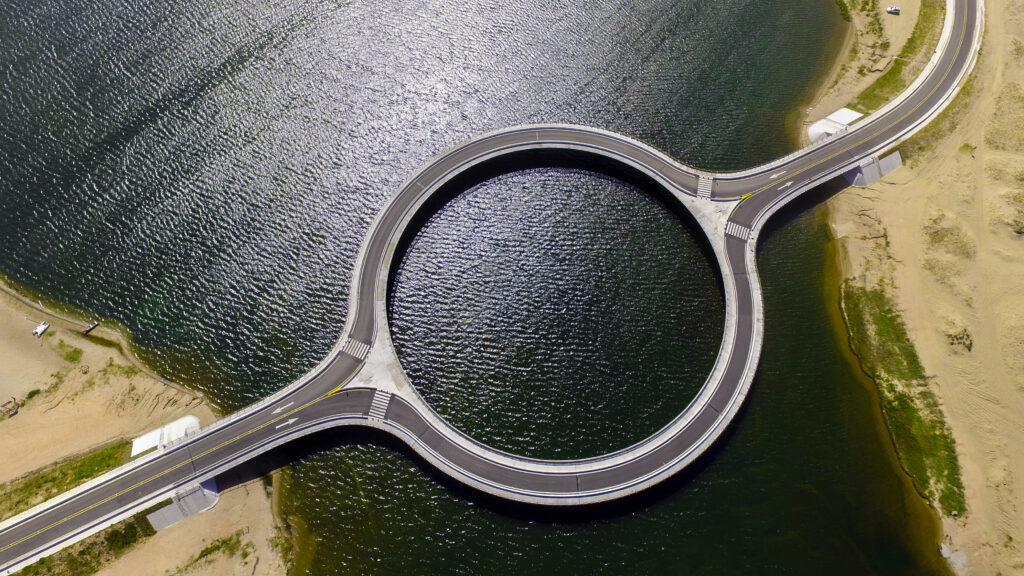 Aerial view of a circular bridge over water, connecting two roads on opposite banks with sandy areas at the edges, highlighting the impact of Infrastructure AI on modern design and connectivity.