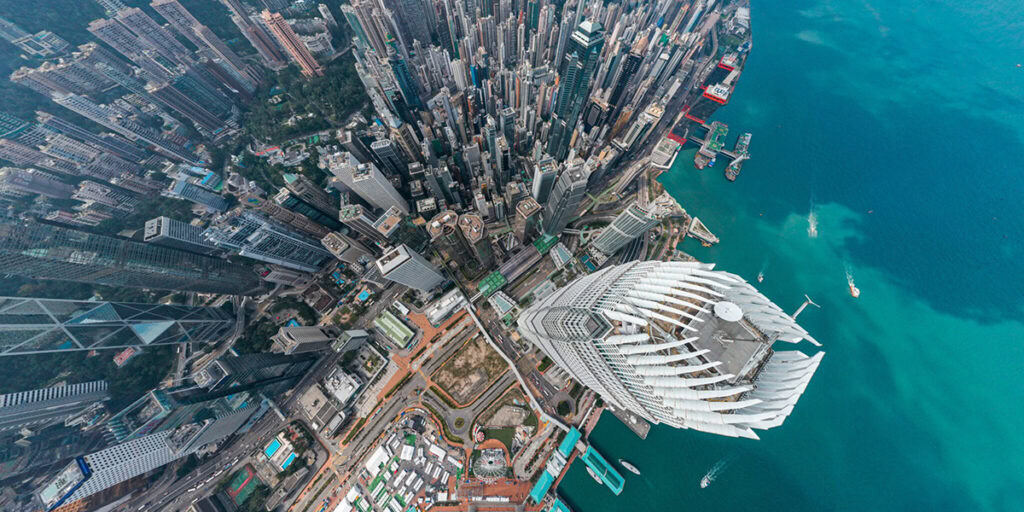 Aerial view of densely packed skyscrapers next to a harbor with clear blue water and boats, illustrating urban density, modern architecture, and the influence of AI in infrastructure development.