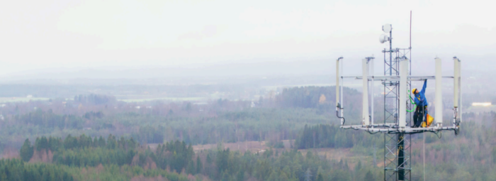 A worker wearing safety gear stands on a tall cellular tower above a foggy, forested landscape—an intrepid global venture captured in one of many real-world user stories.
