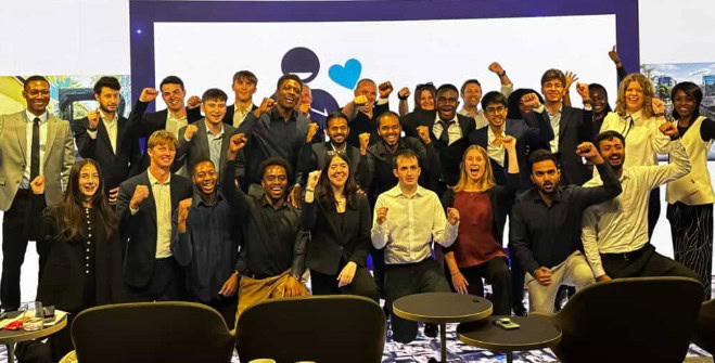 A group of around 30 people in business attire pose together indoors, smiling and raising their fists in celebration—showcasing their enthusiasm for career building and collective achievement.