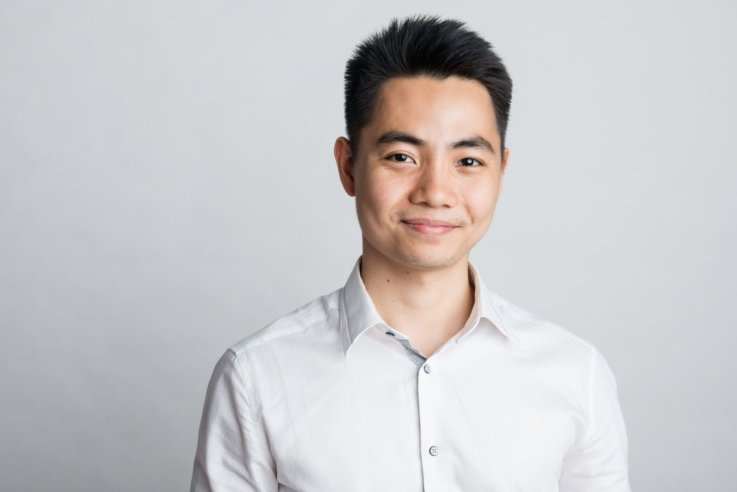 A man with short black hair wearing a white button-up shirt stands against a plain light gray background, smiling slightly for this Bimeco Partner Spotlight.