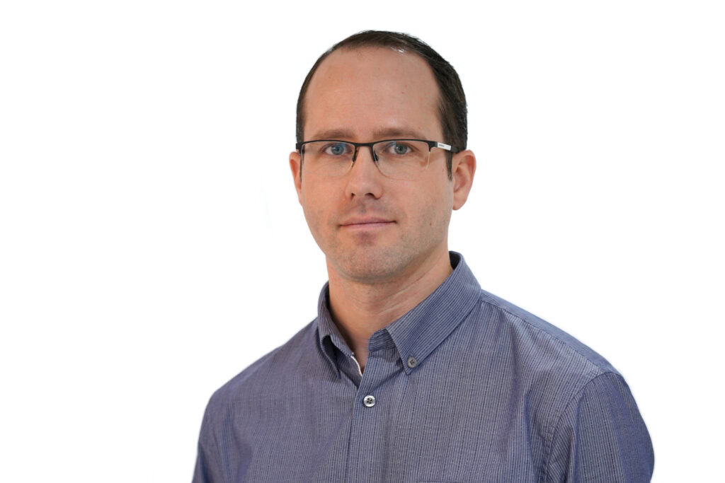 Mężczyzna z krótkimi ciemnymi włosami i w okularach, ubrany w jasnoniebieską koszulę zapinaną na guziki, stoi przodem na jednolitym białym tle – reprezentując profesjonalizm zespołu Bentley.